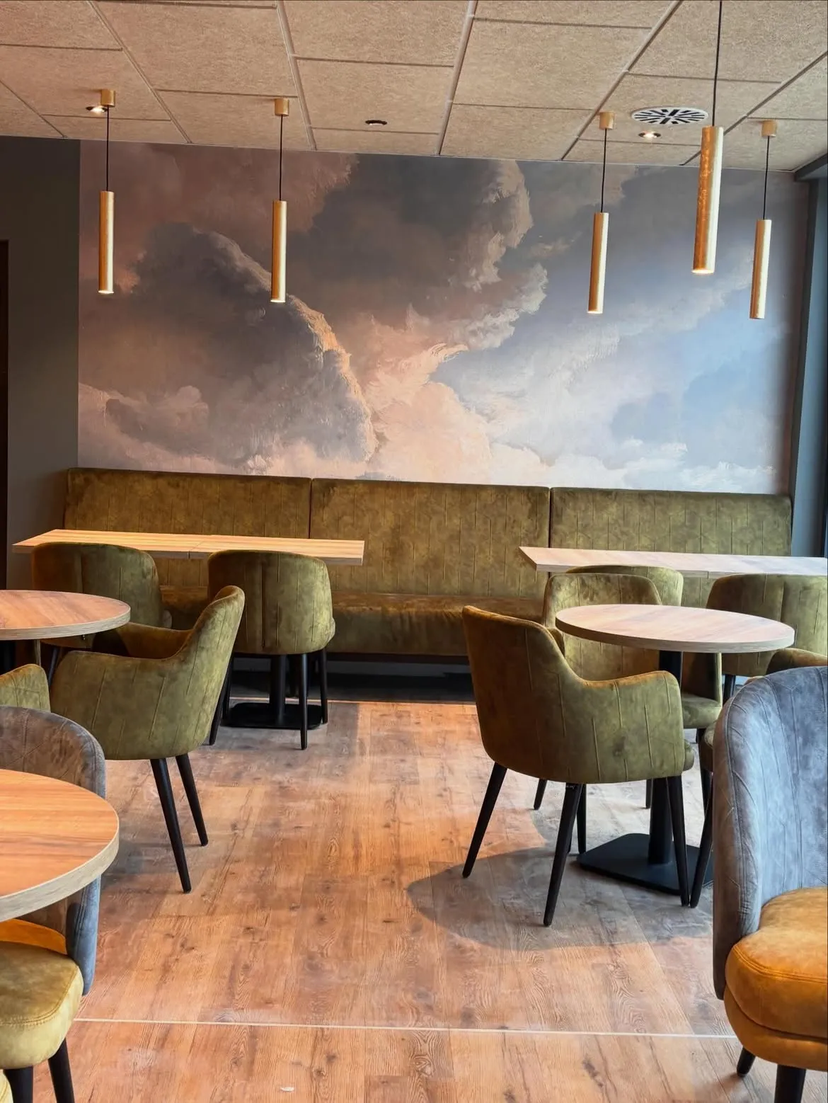 Sitzbereich im neuen Café von Bäcker Chris mit Wolken-Wandbild, olivgrünen Sesseln und warmem Licht